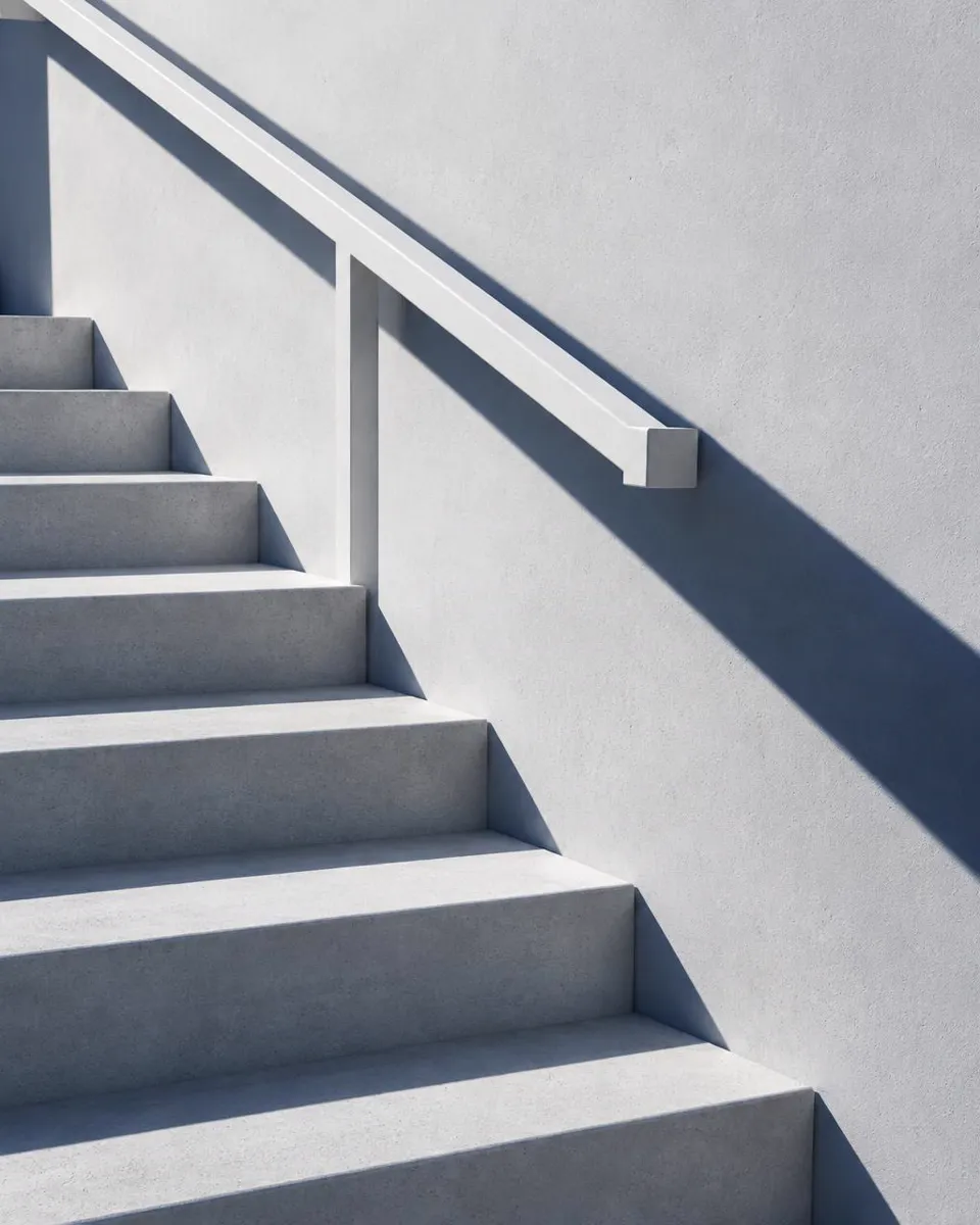 Architectural detail: a white concrete stair and handrail with a long shadow